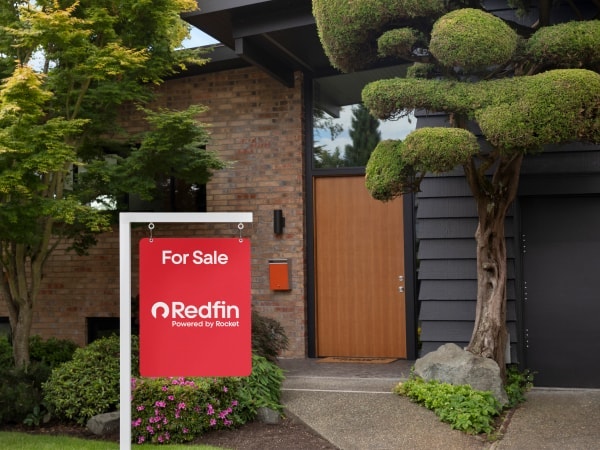 The exterior of a modern house with a large Zillow yard sign